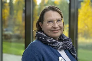 Tiina Nakari Setälä smiling at the camera, she is wearing glasses and a blue cardigan