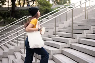 young woman with a bag climbing stairs coffee in hand