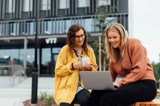 Two VTTers in front of VTT FutureHub with a laptop.