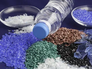 A photo of a plastic bottle surrounded by different colored plastic pellets.