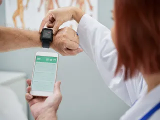 A patient and doctor are examining the readouts from a smartwatch and a smartphone.