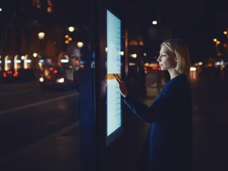 A photo of a person using a touch screen information board in a dark city setting.