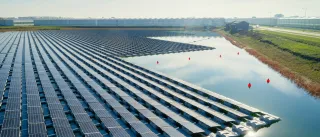 A large amount or solar panels are floating on water used for irrigation in front of rows of greenhouses
