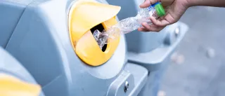 Hand inserting plastic bottle into recycling bin