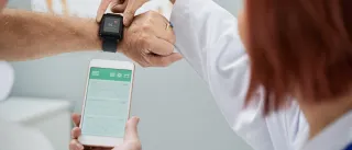 A patient and doctor are examining the readouts from a smartwatch and a smartphone.