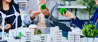 Trio of businesspeople, including a middleaged Asian man and woman, strategize at their desk, prioritizing sustainability renewable energy adoption, waste reduction, and ecofriendly practices.