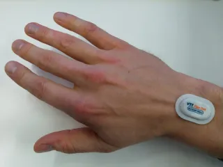 Hand with a small sticker sensor attached to the wrist